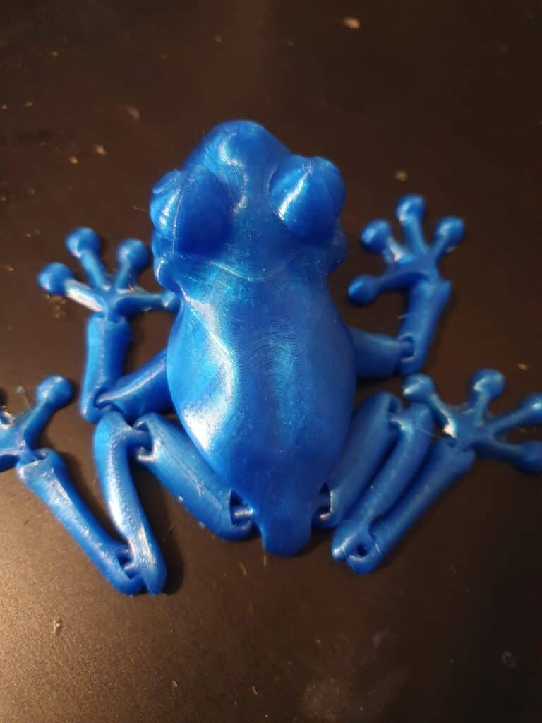 Blue 3D-printed frog model on dark surface.