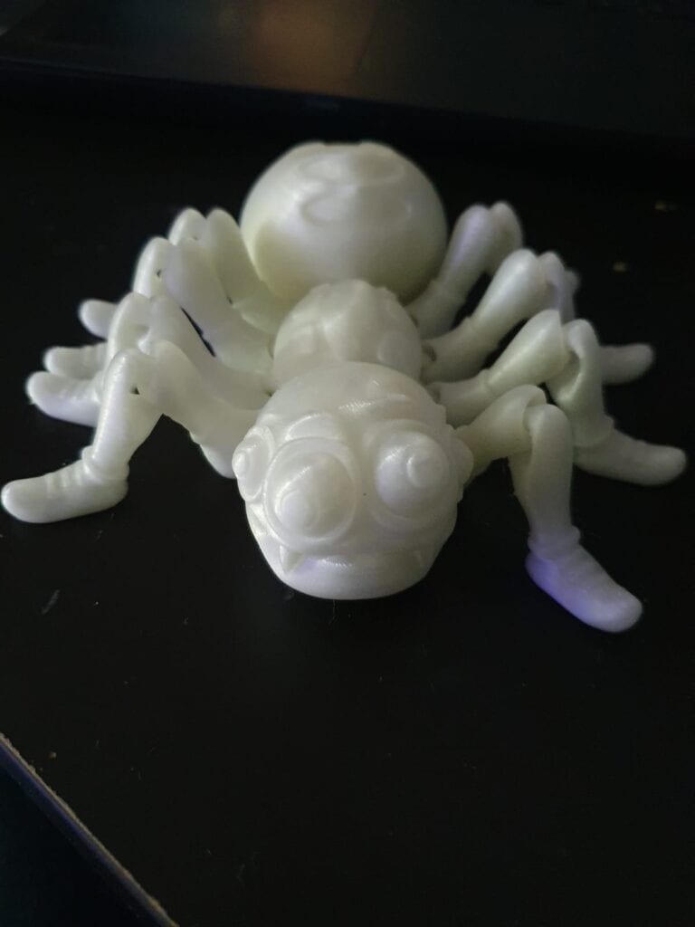 3D-printed white spider model on dark surface.