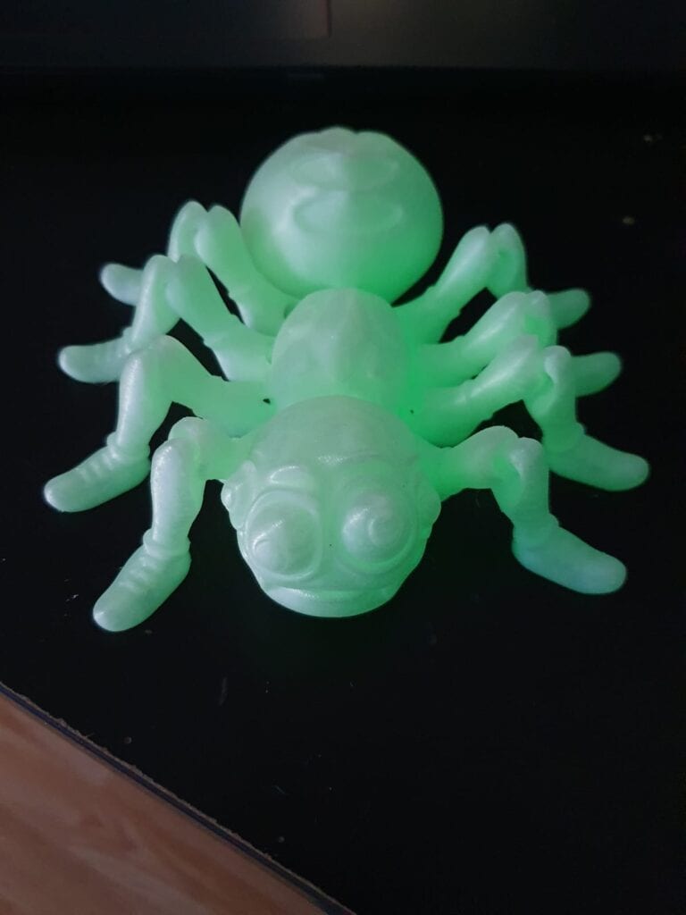 Glow-in-the-dark plastic spider toy on dark surface.