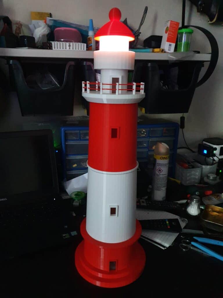 Model lighthouse with illuminated top on cluttered desk.