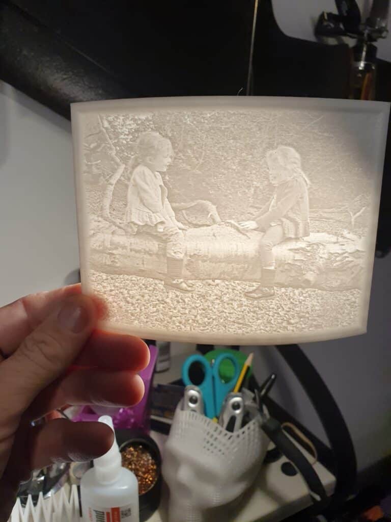 Hand holding lithophane lamp with children's park scene.