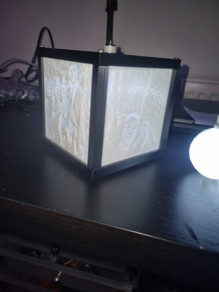 Illuminated 3D-printed photo cube on desk.