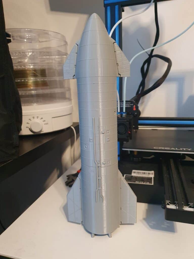 Grey model rocket on office shelf near 3D printer.