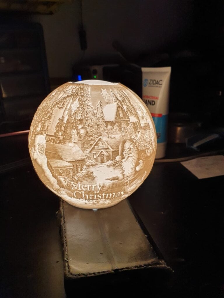 Illuminated Christmas-themed carved wooden orb decoration.