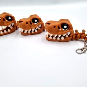 Three brown dinosaur skull keyrings with large cartoon eyes