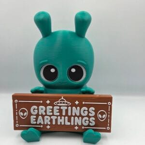 Teal alien figurine holding a Greetings Earthlings sign